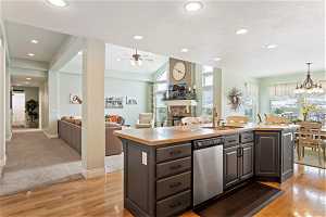 Kitchen with a stone fireplace, a center island with sink, light hardwood / wood-style floors, and stainless steel dishwasher