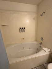 Bathroom featuring a combined bath / shower with jetted tub, tile patterned floors, and toilet