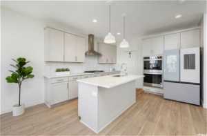 Kitchen featuring double oven, white fridge, wall chimney range hood, tasteful backsplash, and light hardwood / wood-style flooring