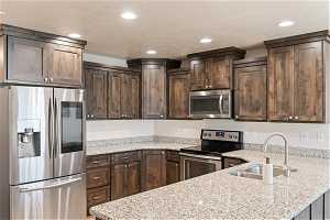 Kitchen with light stone countertops, kitchen peninsula, stainless steel appliances, sink, and dark brown cabinetry