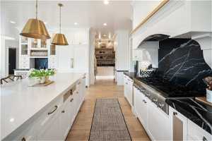 Kitchen with backsplash, light hardwood / wood-style floors, stainless steel gas cooktop, white cabinets, and pendant lighting