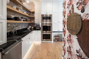 Kitchen with light hardwood / wood-style flooring, white cabinetry, backsplash, appliances with stainless steel finishes, and sink