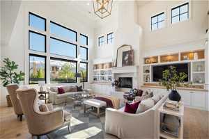 Living room featuring a large fireplace, light wood-type flooring, plenty of natural light, and a towering ceiling