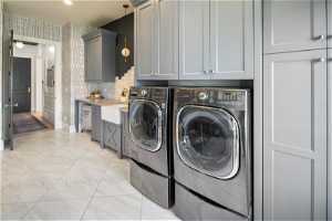 Clothes washing area featuring cabinets, sink, light tile floors, and washer and clothes dryer