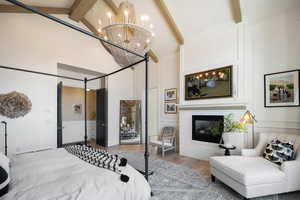 Bedroom featuring wood-type flooring, beamed ceiling, high vaulted ceiling, a brick fireplace, and a notable chandelier