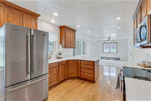 Kitchen featuring ceiling fan, stainless steel appliances, kitchen peninsula, light hardwood / wood-style flooring, and a baseboard radiator