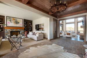 Living area featuring a wooden ceiling with exposed beams, stone finish floors, a chandelier, a fireplace, and built in features