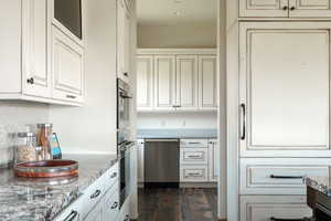 Kitchen featuring cream cabinetry, stainless steel appliances, dark wood finished floors, backsplash, and light stone countertops