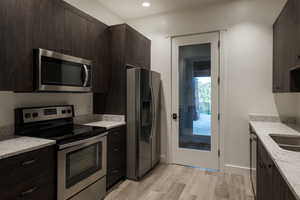 Kitchen featuring stainless steel appliances, light wood-style flooring, dark brown cabinetry, light stone countertops, and recessed lighting