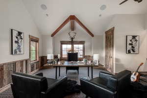 Carpeted home office with wainscoting, ceiling fan, vaulted ceiling, plenty of natural light, and wood walls