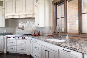Kitchen with stainless steel gas stovetop, glass insert cabinets, under cabinet range hood, and decorative backsplash