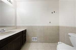 Bathroom featuring vanity, toilet, tile floors, and tile walls