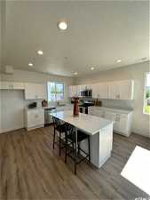 Kitchen featuring appliances with stainless steel finishes, wood-type flooring, white cabinets, sink, and a center island
