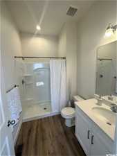 Bathroom with hardwood / wood-style flooring, toilet, vanity with extensive cabinet space, and a shower with curtain