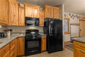 Kitchen featuring light stone counters, light tile floors, and black appliances