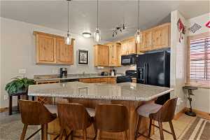 Kitchen featuring pendant lighting, black appliances, a kitchen bar, and light stone countertops
