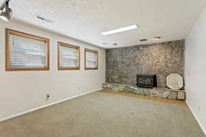 Interior space with a textured ceiling, carpet floors, a fireplace, and a wood stove