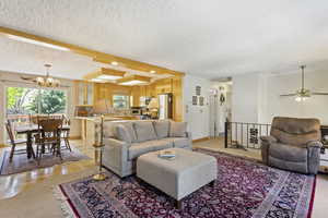 Living room with ceiling fan with notable chandelier, a textured ceiling, and beamed ceiling