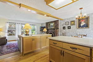 Kitchen with a brick fireplace, a textured ceiling, light wood-type flooring, decorative light fixtures, and a chandelier