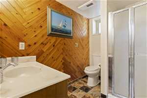 Bathroom with a textured ceiling, walk in shower, toilet, wood walls, and vanity