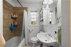 Full bathroom featuring a wealth of natural light, tile floors, toilet, and shower / bath combo with shower curtain