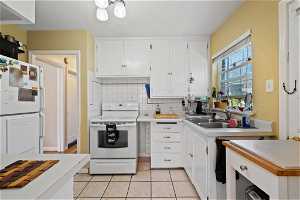Kitchen with white appliances, light tile flooring, white cabinetry, backsplash, a