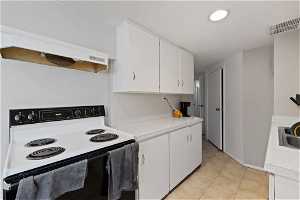 Kitchen featuring white electric stove, premium range hood, white cabinets, and light tile floors
