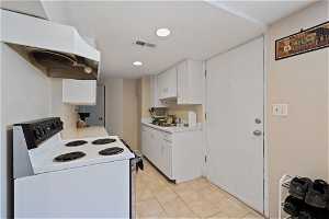 Kitchen with premium range hood, white cabinetry, light tile flooring, and white range with electric stovetop