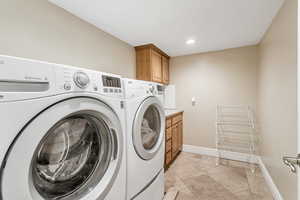 Clothes washing area featuring washer and clothes dryer, cabinets, and light tile flooring