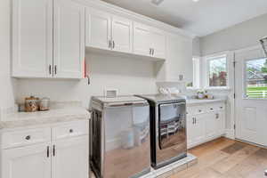 Washroom with washing machine and dryer, cabinets, and light wood-type flooring