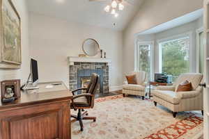 Home office with a stone fireplace, lofted ceiling, ceiling fan, and hardwood / wood-style flooring