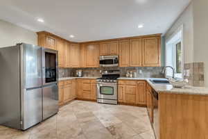 Kitchen featuring light stone counters, appliances with stainless steel finishes, backsplash, and sink