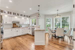 Kitchen with white cabinets, pendant lighting, light wood-type flooring, and custom range hood