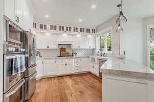 Kitchen with premium range hood, light hardwood / wood-style floors, kitchen peninsula, and white cabinets