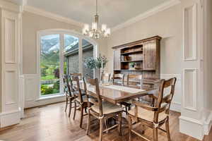 Dining room with light hardwood / wood-style flooring, crown molding, and an inviting chandelier