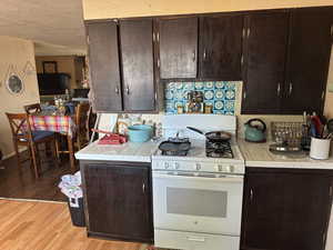 Kitchen with white gas range oven, a textured ceiling, light hardwood / wood-style flooring, dark brown cabinets, and tile counters