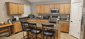 Kitchen featuring appliances with stainless steel finishes, lofted ceiling, light tile flooring, and a kitchen island