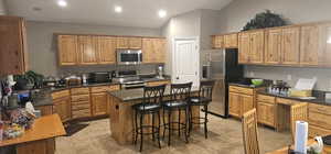 Kitchen featuring dark stone counters, light tile flooring, stainless steel appliances, a center island, and lofted ceiling