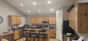 Kitchen featuring dark stone counters, light tile flooring, stainless steel appliances, a center island, and lofted ceiling