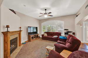 Living room with a premium fireplace, light carpet, ceiling fan, and lofted ceiling