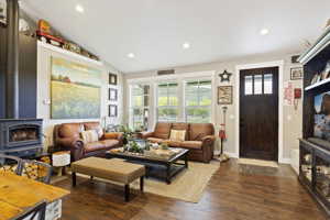 Living room featuring dark hardwood floors, a wood stove, and vaulted ceiling