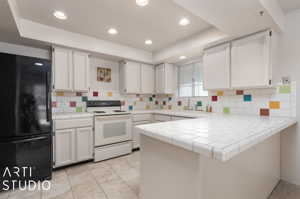Kitchen with kitchen peninsula, black refrigerator, white range with electric cooktop, white cabinetry, and tile countertops