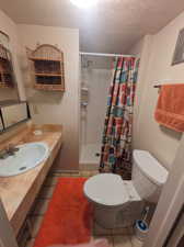 Bathroom with vanity with extensive cabinet space, toilet, tile flooring, walk in shower, and a textured ceiling