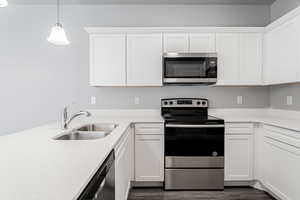 Kitchen featuring white cabinets, appliances with stainless steel finishes, pendant lighting, and sink