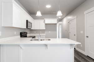 Kitchen with white cabinets, pendant lighting, sink, and electric stove