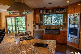 Kitchen featuring stainless steel double oven, light stone counters, and wall chimney exhaust hood