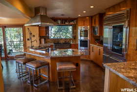 Kitchen featuring appliances with stainless steel finishes, tasteful backsplash, dark tile flooring, wall chimney exhaust hood, and light stone counters