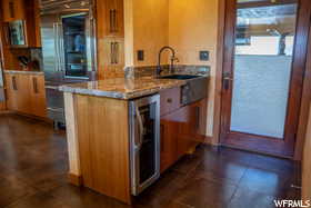 Kitchen featuring stone counters, dark tile flooring, sink, and beverage cooler