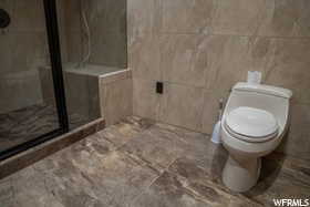 Bathroom featuring an enclosed shower, toilet, and tile flooring