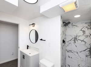 Bathroom featuring a tile shower, vanity, and toilet